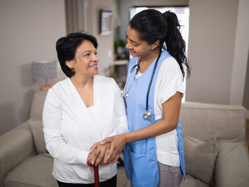 Young nurse standing with female patient at home